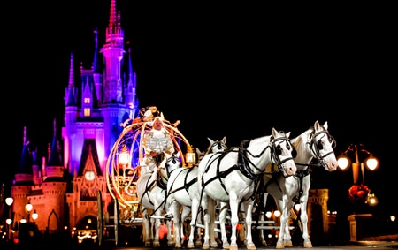 A coachman in Cinderella's Crystal Coach drives 6 horses outside Cinderella Castle at night