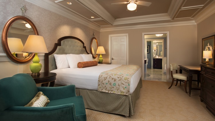 A bedroom with a bed, quilted headboard, armchair, mirrors and a dresser