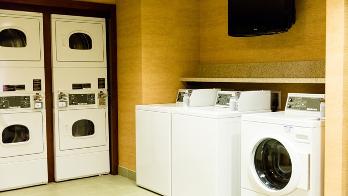 A stacked washer and dryer in a laundry room with cupboards and shelves